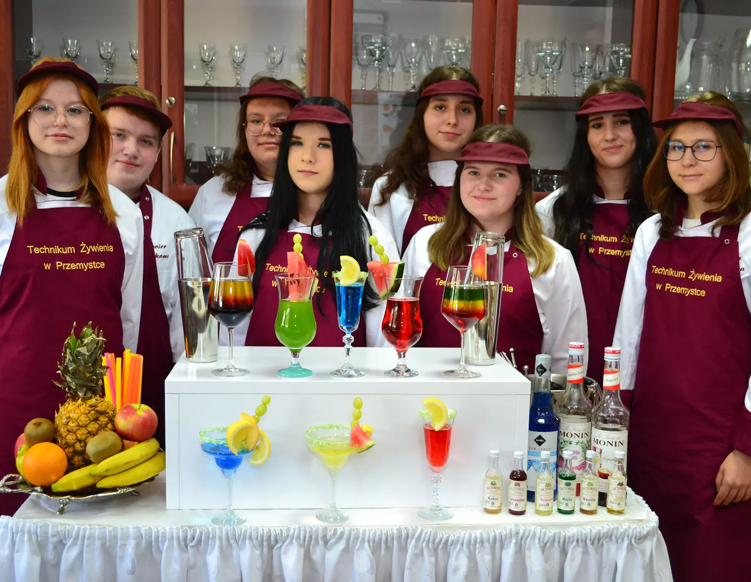 Uczniowie kierunku Technik Żywienia i Usług Gastronomicznych za barkiem, na którym stoją kolorowe napoje